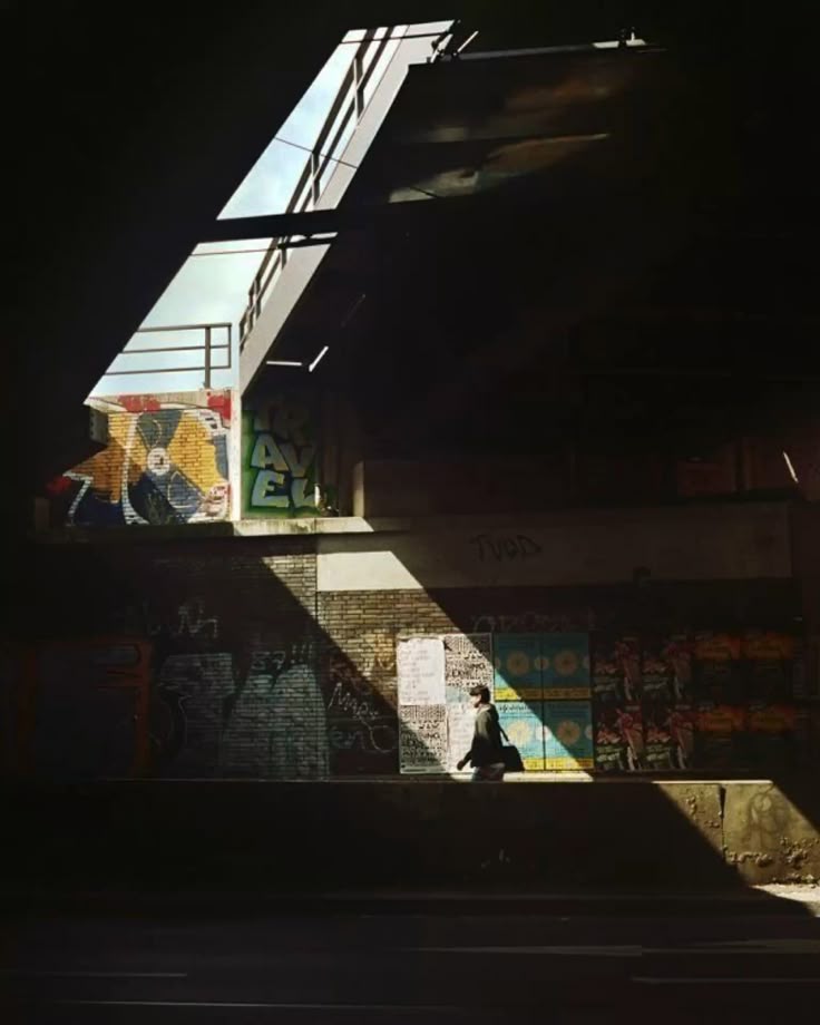 A lone figure crossing a shaft of daylight under dark concrete architecture